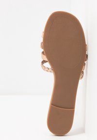Semelle d’une sandale marron avec une prise texturée, montrant des lanières tressées et lisses sur fond blanc.