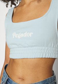 Jasnoniebieski krótki top wykonany z miękkiej bawełny, z kwadratowym dekoltem i zgromadzonym elastycznym pasem w talii, z napisem "Pegador" w kolorze białym.