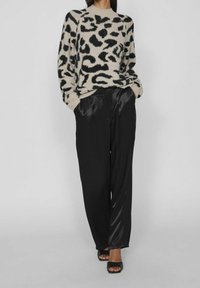 Tiermuster-Pullover in Beige und Schwarz mit weicher Textur, kombiniert mit schwarzen satinweiten Hosen und schwarzen Sandalen.