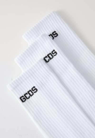 Chaussettes blanches côtelées avec le logo noir "GCDS". Le design comprend une longueur mi-mollet et une texture lisse, mettant en avant un style minimaliste.