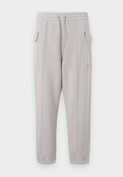 Γκρι φόρμες με ελαστική μέση, πλαϊνές τσέπες και ραφή που τρέχει κάθετα κατά μήκος των ποδιών. Υφασμάτινη σύνθεση από βαμβάκι.