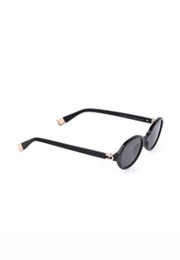 Lunettes de soleil noires à monture ronde avec verres teintés et accents dorés sur les branches et les charnières, présentées sur un fond blanc.