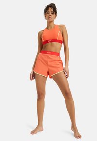 Ljusröd sportbh och matchande shorts med röda accenter och en logotyp. Tillverkad av ett smidigt, elastiskt material; har en figurnära design.