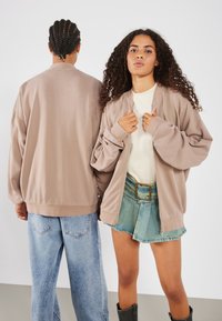 Light beige oversized bomber jackets with dropped shoulders, paired with distressed blue denim jeans and a blue denim mini skirt.