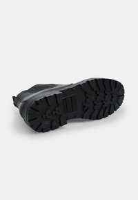 Suela de zapato de goma negra con profundas huellas para una buena tracción. Tacón ligeramente redondeado y superficie texturizada. Diseño plano y ancho para mayor estabilidad.
