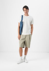 Hvit T-skjorte med korte ermer, lysebeige shorts, denim tote bag, hvite sneakers, og hvite ankelsokker. Enkel design, avslappet passform.