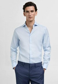 Camisa de vestir azul claro de algodón con cuello amplio, frente con botones y mangas largas, combinada con pantalones oscuros azules.