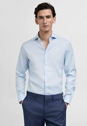 Light blue dress shirt in cotton fabric with a spread collar, button-down front, and long sleeves, paired with dark blue trousers.