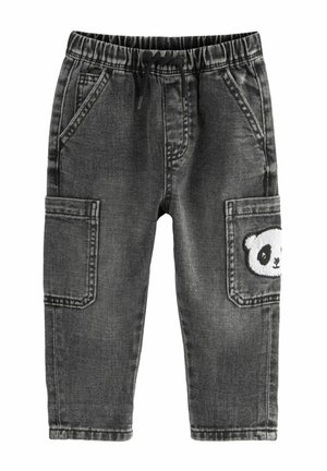 Enfant portant un t-shirt rayé noir et blanc, un pantalon en jean gris avec un patch panda et des baskets blanches, debout sur un sol clair.