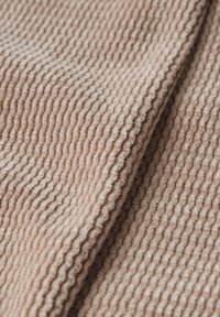Tissu beige côtelé affichant des rainures texturées, une surface douce et des épaisseurs variées, plié pour révéler des détails superposés et de la profondeur.