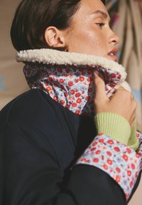 Palton bleumarin cu guler și manșete cu model floral. Căptușeală moale și texturată care contrastează cu țesătura exterioară netedă. Manșete verzi cu dungi adaugă detaliu.