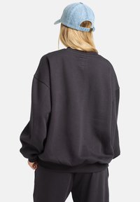 Felpa ampia grigio scuro con polsini e orlo a coste, realizzata in tessuto morbido. Abbinata a un cappellino in denim azzurro.