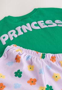 Camisa verde con la palabra "PRINCESS" en letras blancas y pantalones cortos de color púrpura claro con un patrón floral colorido.