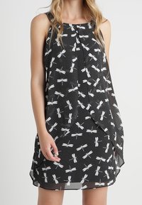 Svart ärmlös klänning med en libellumönster i vitt, på en prickig bakgrund och en lös, flödande siluett.