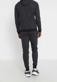Chándal deportivo gris oscuro que incluye una chaqueta con capucha y pantalones de chándal ajustados con puños acanalados, hechos de una tela suave, diseñado para mayor comodidad.