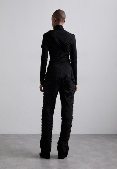 Ensemble noir comprenant un haut ajusté avec des détails froncés et un col haut, associé à un pantalon plissé à motifs avec une texture superposée.