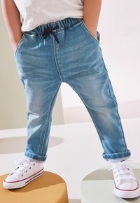Pantalons en denim bleu clair avec une taille élastique, cordon de serrage, poches latérales et ourlets retroussés, associés à des baskets blanches.