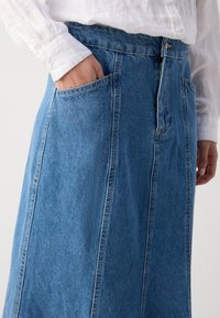 Lichblauwe spijkerrok met een hoge taille, zijzakken en zichtbare stiksels. De stof heeft een gestructureerde uitstraling, die typisch is voor spijkerstof.