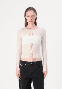 Lett, ribbestrikket topp i krem og hvit med lange ermer, et nøkkelhull foran, justerbare knytesnorer og sideslisser ved ermene.