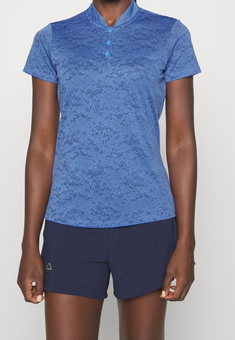 Polo bleu à manches courtes avec un motif texturé et un col montant, doté de trois boutons au niveau du col. Associé à un short bleu marine.