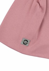 Indumento in tessuto rosa con una texture liscia. Presenta una toppa quadrata in grigio, etichettata "mikk-line", posizionata in basso.