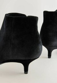 Stivaletti neri in suede presentano un design elegante con un tacco affusolato di 3 pollici. La texture è liscia, con dettagli minimi e una punta arrotondata.