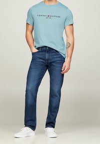 Světle modré bavlněné tričko s logem, doplněné o tmavě modré džíny a bílé tenisky. Standardní střih s krátkými rukávy a kulatým výstřihem.