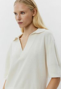 Lichtcrème oversized trui met een V-hals, korte mouwen en een zachte textuur. Bevat een platte kraag en subtiele zijsplitten.