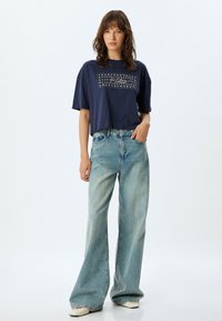 Camiseta corta de color azul marino con un gráfico de estrellas. Combinada con unos vaqueros de pierna ancha de color azul claro, creando una silueta relajada.