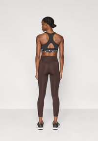 Brassière de sport athlétique noire avec un dos échancré en forme de goutte et une bande de marque, associée à des leggings marron, à la texture lisse et longueur cheville.