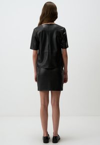 Top in pelle nera con maniche corte e zip sul retro, abbinato a una mini gonna in pelle nera. Texture liscia.