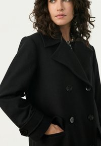 Palton negru din lână cu un design cu nasturi dubli, rever mari și textură netedă. Are nasturi rotunzi negri și buzunare laterale.