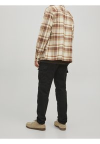 Brown and cream plaid flannel shirt, buttoned cuffs, paired with black cargo pants and beige shoes. Simple, functional design.