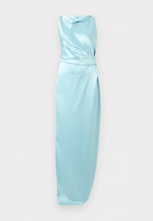 Kobieta w jasnoniebieskiej, bezrękawnikowej sukni satynowej z bocznym rozcięciem, stojąca z jedną ręką na biodrze, nosząca czarne sandały na wysokim obcasie z paskami wokół kostki.