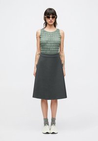 Groen getextureerd mouwloos topje gecombineerd met een donkergroene A-lijn rok, gedragen met witte sportschoenen en grijze enkelsokken.