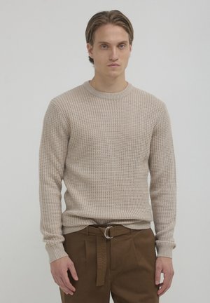 Beige textured knit sweater with ribbed crewneck and cuffs, paired with brown belted trousers. Simple design, casual fit.