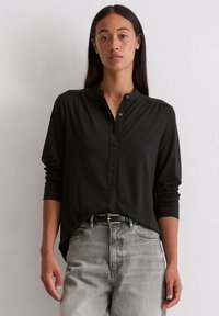Chemise noire à manches longues avec un col rond, un devant à boutons et des détails froncés aux épaules. Associe avec un jean gris clair taille haute.