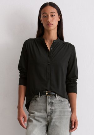 Zwarte longsleeve shirt met een ronde kraag, knopen aan de voorkant en geplooide schouderdetails. Gecombineerd met lichtgrijze hoge taille jeans.