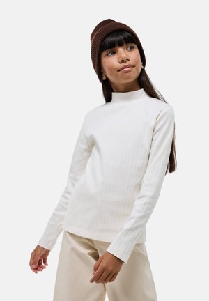 Haut à manches longues blanc côtelé avec un col montant, associé à un pantalon beige à jambes larges et un bonnet en tricot brun côtelé.