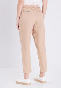 Beige linnen broeken met een relaxte pasvorm, elastische tailleband, zijzakken en twee achterzakken met rits. Gemaakt met witte sneakers.