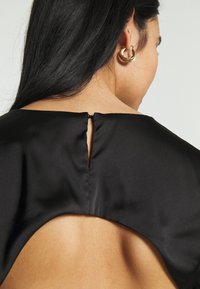 Černý saténový top s klíčovou dírkou na zadní straně, s hladkou texturou a elegantním střihem, který zvýrazňuje ramena.