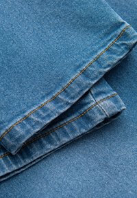 Tissu en denim bleu plié avec des coutures orange contrastantes, présentant une texture lisse et un design classique de jeans.