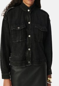 Giubbotto in denim nero con colletto rialzato, due tasche frontali e bottoni a pressione. Tessuto testurizzato con un motivo sottile. Vestibilità aderente in vita.