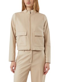 Beżowa krótka kurtka z wysokim kołnierzem, pełnym suwakiem z przodu oraz dwoma kieszeniami na piersi; wykonana z gładkiej, lekkiej tkaniny.