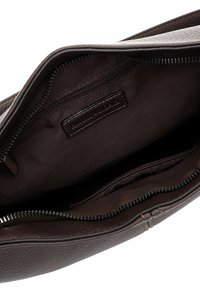 Interno della borsa in pelle marrone con finitura texturizzata, dotato di una tasca con zip, foderato in tessuto e con un dettagli di etichetta cucita.