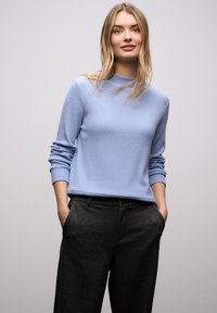 Jasnoniebieski prążkowany sweter z dzianiny z długimi rękawami, zestawiony z ciemnoszarymi spodniami o luźnym kroju i prostym designie.