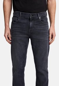 Jeans in denim scuro con taglio dritto, leggera scoloritura, cinque tasche e chiusura frontale con bottone. Il tessuto ha una texture liscia.