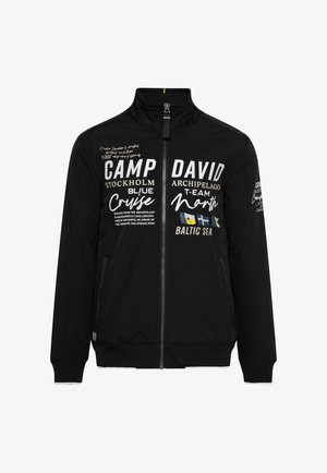 Schwarze Zip-Up-Jacke mit hohem Kragen. Verfügt über weiße und graue Textelemente sowie gestreifte Bündchenabschlüsse. Zwei Seitentaschen.