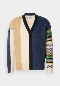 Cardigan med blandede teksturer i beige, navy og creme, med dristige grønne og blå mønstrede ærmer og en v-udskæring. Seks sorte knapper.