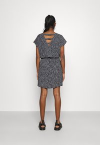 Robe à motifs floraux bleu marine avec des manches courtes, taille élastique et détail dos croisé. Longueur au-dessus du genou, associée à des sandales noires.